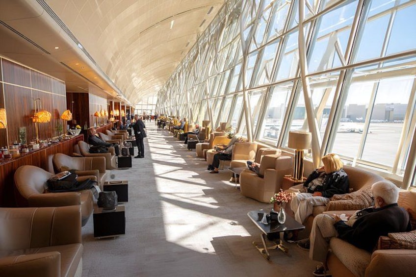 Eine großzügige Flughafenlounge mit Ledersitzgelegenheiten, Tischen und großen Fenstern. 2