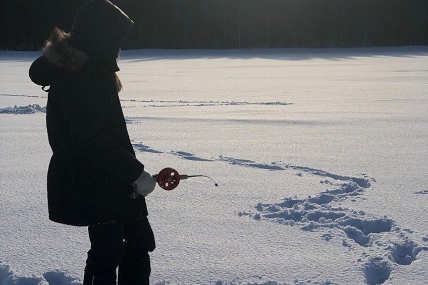 A person in a dark coat holding a red object, standing on snow-covered ground with footprints. 2