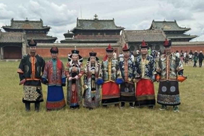 A group of people in traditional attire standing in a field with traditional architecture in the background. 1