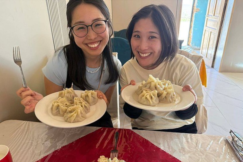 Two people holding plates of dumplings at a table with a red tablecloth. 4