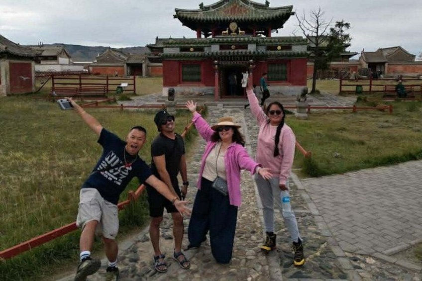 A group of people posing in front of a traditional building with a tiled roof and red walls. 2