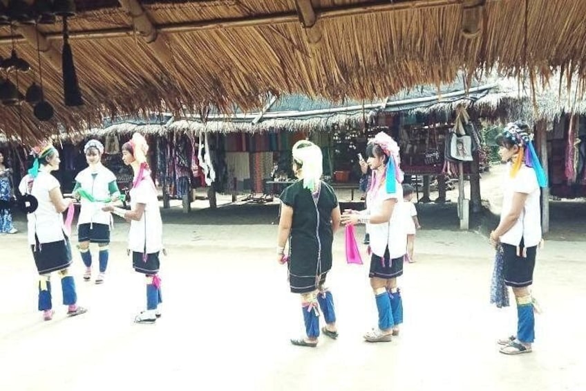A group of people in traditional attire standing in a thatched-roof structure. 4