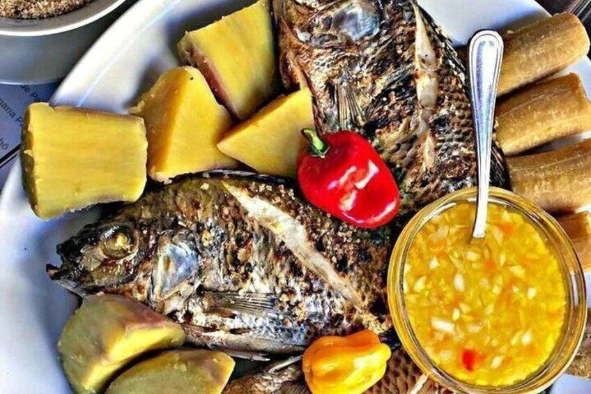 Grilled fish, slices of yellow fruit, a red chili pepper, and a bowl of yellow sauce. 2