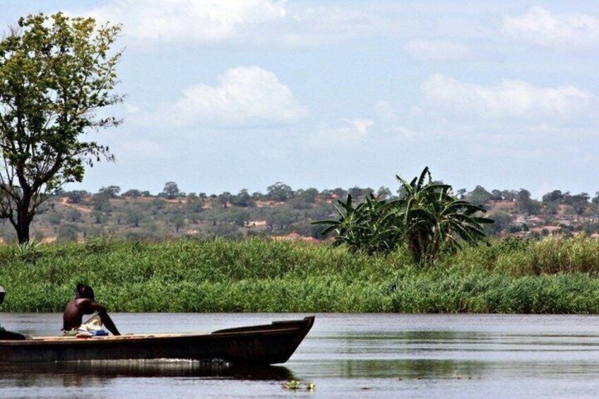 A person in a boat on a calm river, surrounded by lush greenery and distant hills. 1