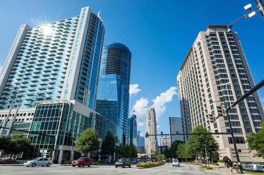A cityscape with modern high-rise buildings, a clear blue sky, and a few cars on the street. 4