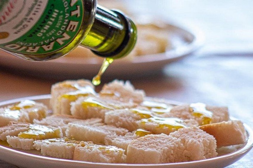 A bottle of olive oil being poured over cubed cheese on a plate. 4
