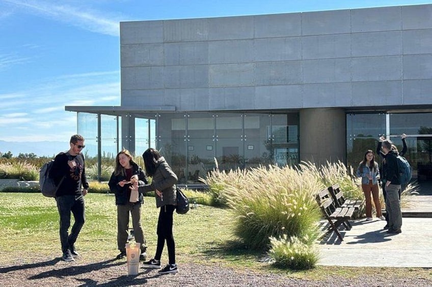A group of people standing outdoors near a modern building with glass windows and a concrete facade. 3