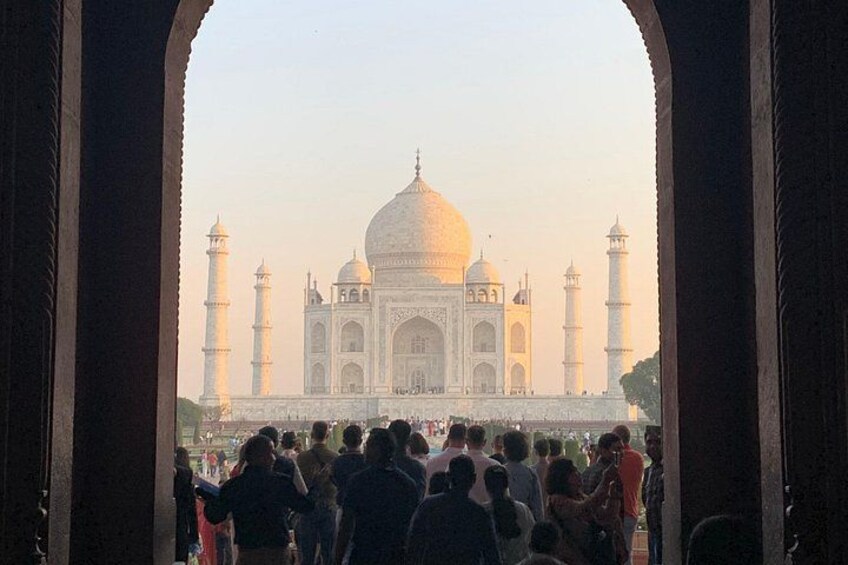 Das Taj Mahal mit vier Minaretten, wie es durch einen Bogen mit Personen im Vordergrund sichtbar wird. 4