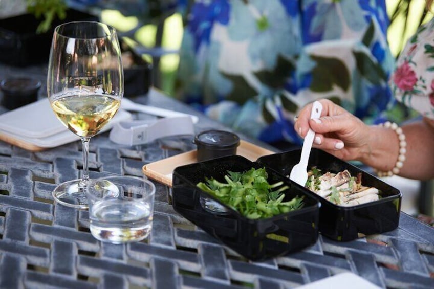 A person eating a salad with a fork, a glass of white wine, and a water glass on a table. 1