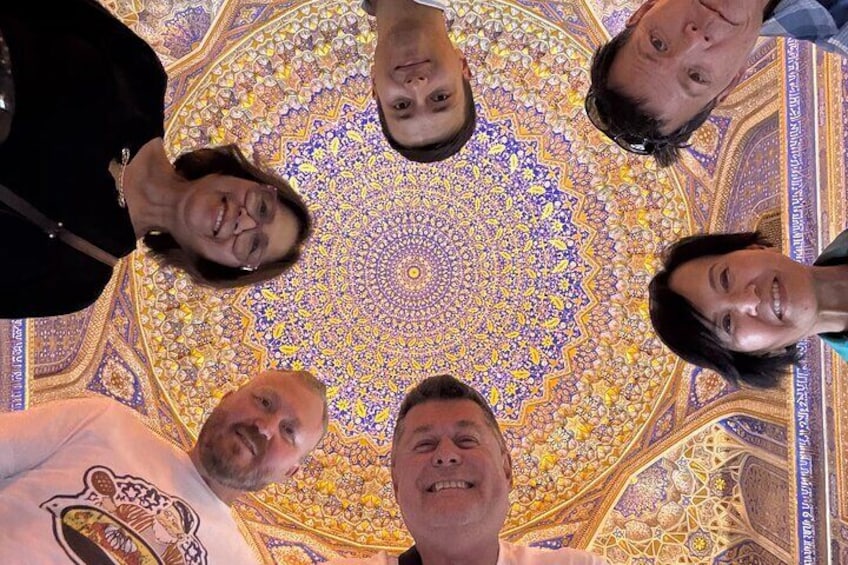 Un groupe de personnes se tient en cercle, sous un plafond orné d’un motif coloré et détaillé. 4