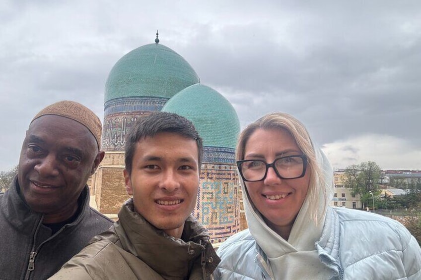 Trois personnes se tiennent devant une mosquée surmontée d’un grand dôme turquoise. 2