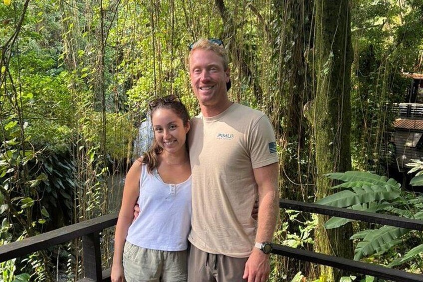 A man and a woman standing on a wooden deck surrounded by dense tropical foliage. 5