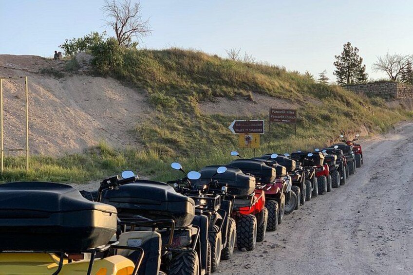 A row of motorcycles parked on a dirt road with a sign indicating a location. 3