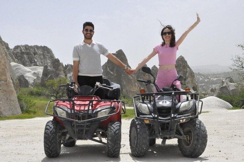 Two people holding hands, standing next to ATVs on a rocky terrain with large boulders and sparse vegetation. 5