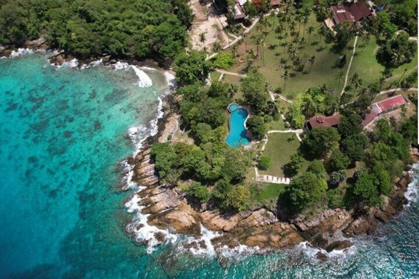 Vue aérienne d’une zone côtière avec une piscine entourée d’arbres et un rivage rocheux. 1