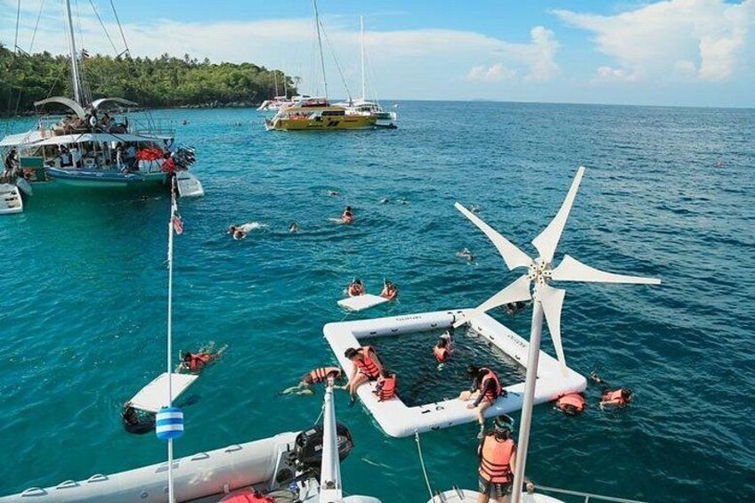 A marina with boats, people swimming, and a wind turbine. 5