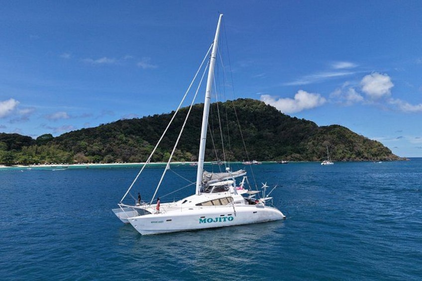 A white sailboat named 'Mojito' on calm blue waters with a forested island in the background. 4