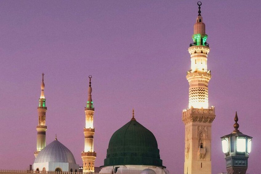 A mosque with illuminated minarets and domes against a purple sky. 1
