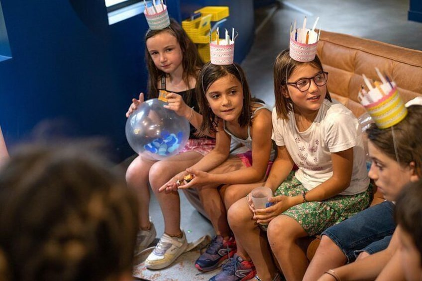 Children sitting on a couch, wearing party hats, and holding a balloon. 2