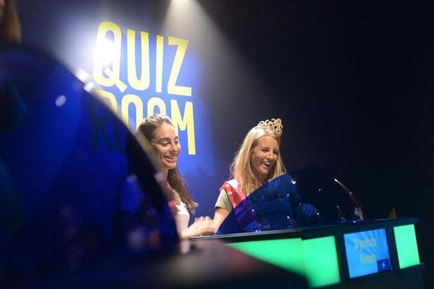 Two people at a podium with a quiz room backdrop. 4