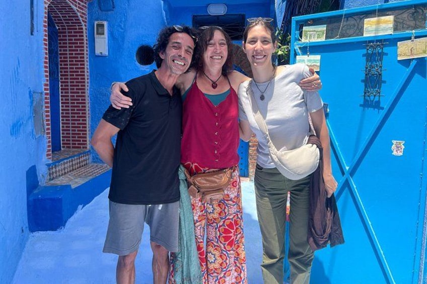 Three people standing in front of a blue building with a red door and a window. 4