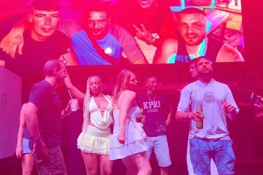 A group of people at a nightclub with a DJ booth and stage lighting. 2