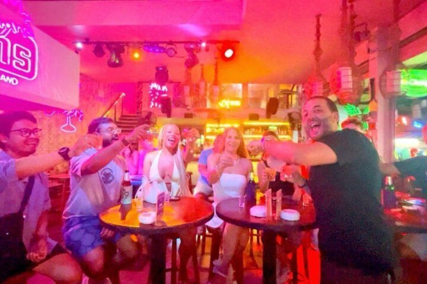 A group of people toasting at a bar with neon signs and festive decorations. 5