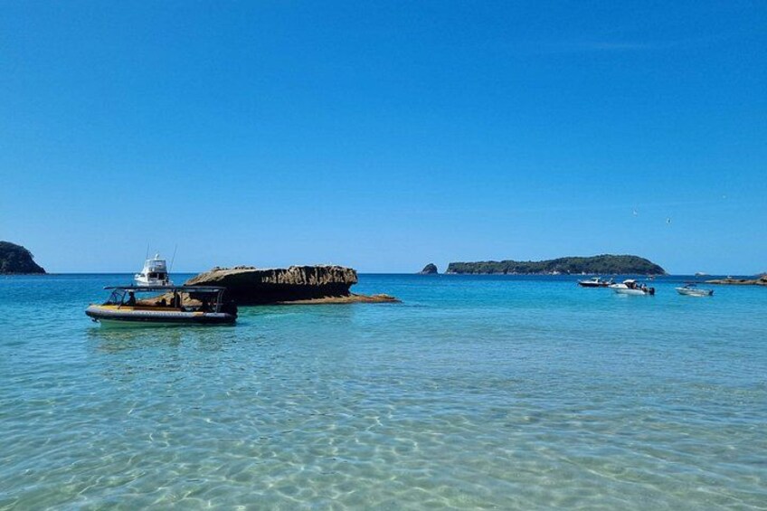 Mar azul cristalina con barcos, un promontorio rocoso y islas a lo lejos. 2