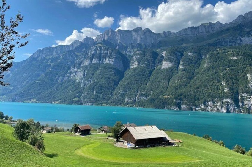 Un paisaje montañoso con un lago, campos verdes y algunos edificios. 2