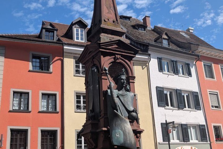 Una estatua de una figura histórica en una plaza, con edificios coloridos al fondo. 3