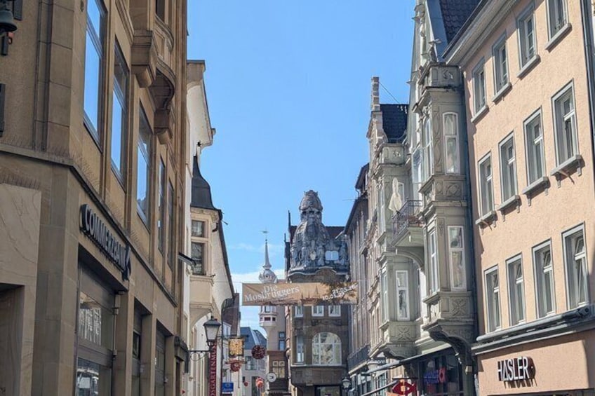 Una calle con edificios históricos, una estatua destacada y un cartel que dice 'HISLER'. 4