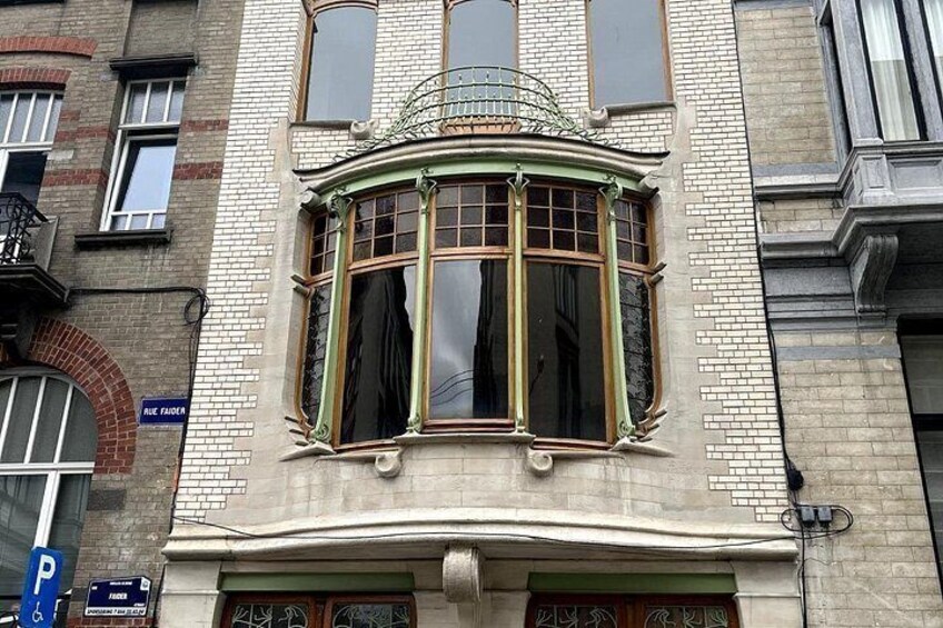 A building with a large bay window, a sign reading 'Rue Faider,' and a blue parking sign. 4