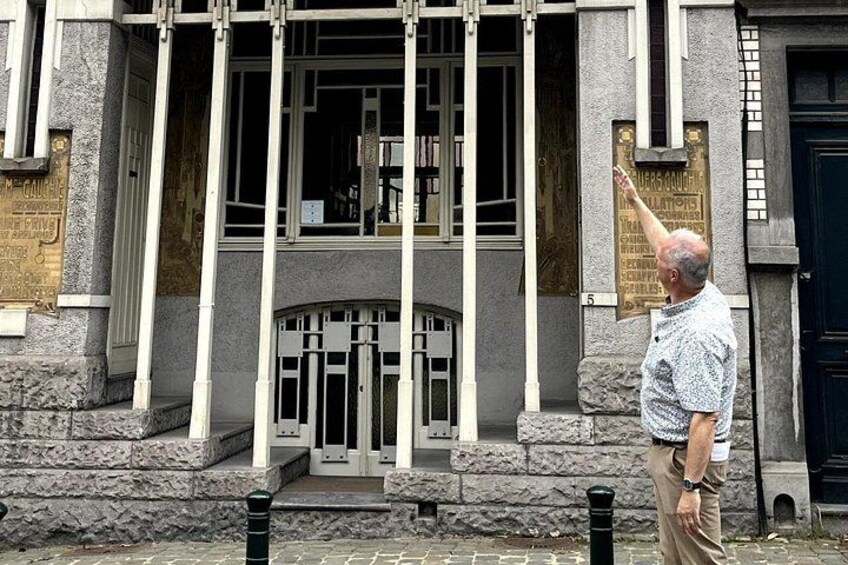Un homme se tient devant un bâtiment orné d’une plaque et flanqué d’un poteau noir. 1