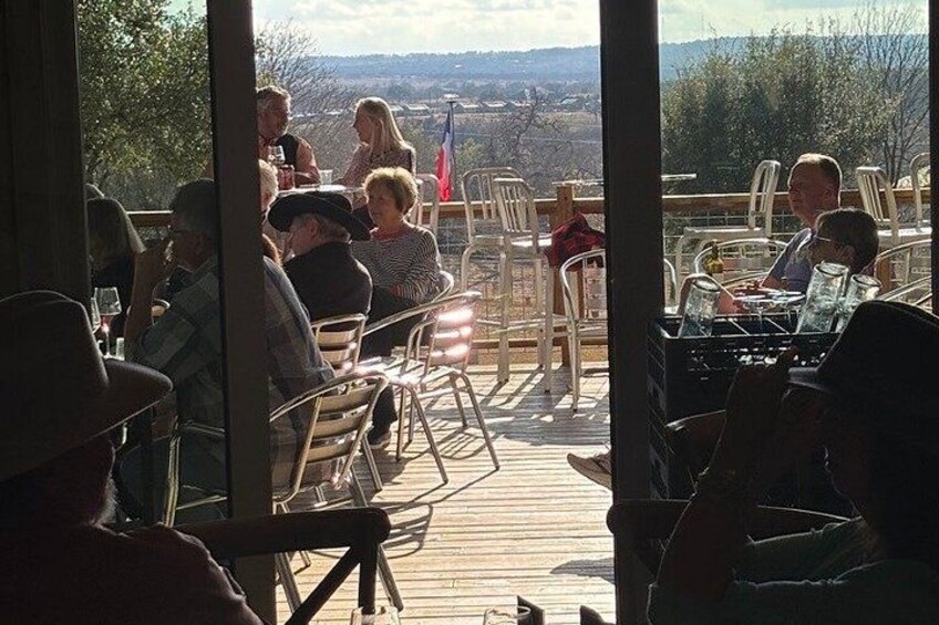 People seated at tables on a wooden deck with a view of a landscape. 3