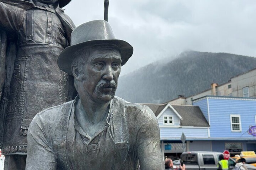 A statue of a man in work clothes and a hat, with a mountain and buildings in the background. 4