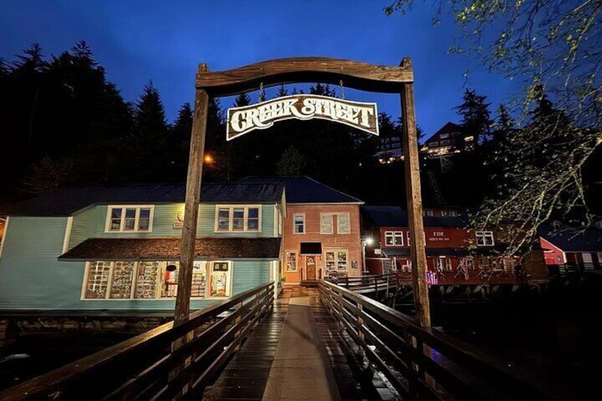 A wooden bridge with a sign reading "Creek Street" leading to a building with a blue facade. 1