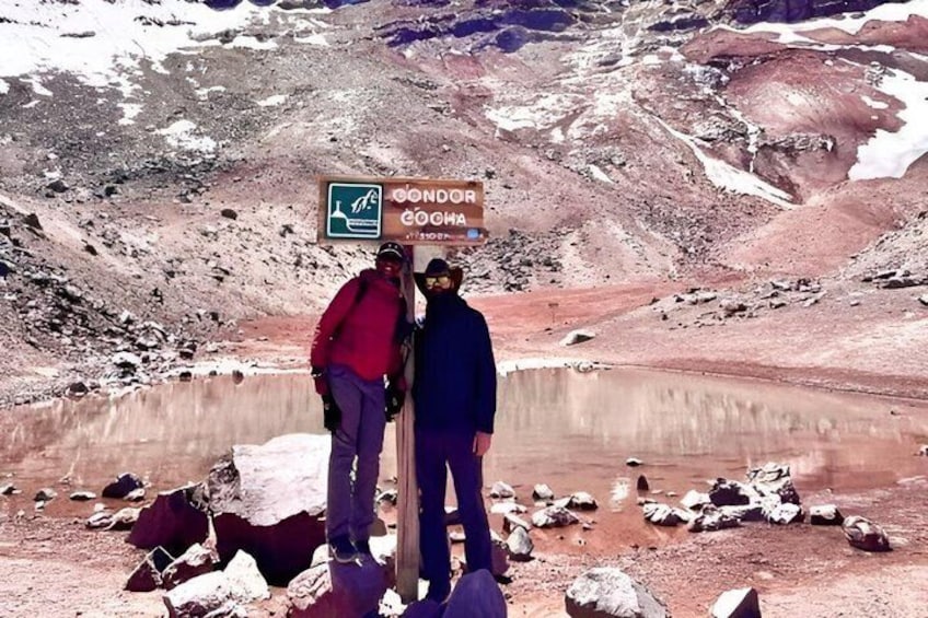 Two people standing by a signpost in a mountainous area with a lake. 2