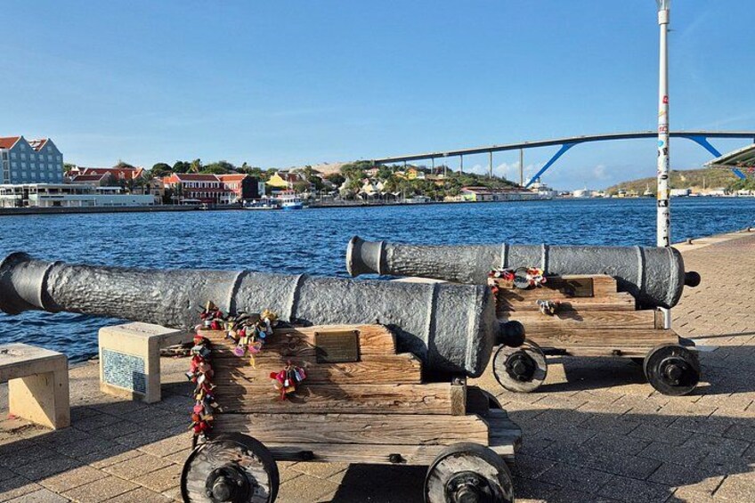 Two cannons on a dock with a bridge and buildings in the background. 3