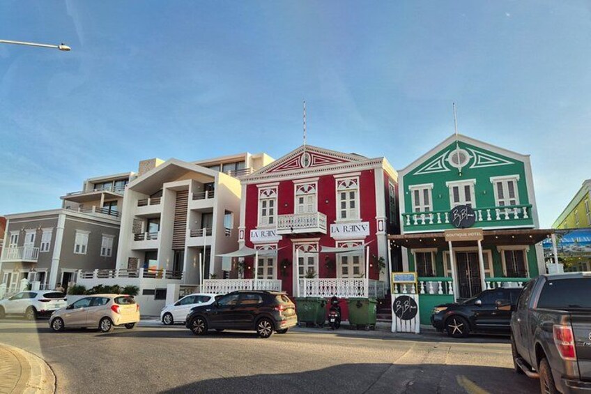 A street with colorful buildings, parked cars, and a clear sky. 5