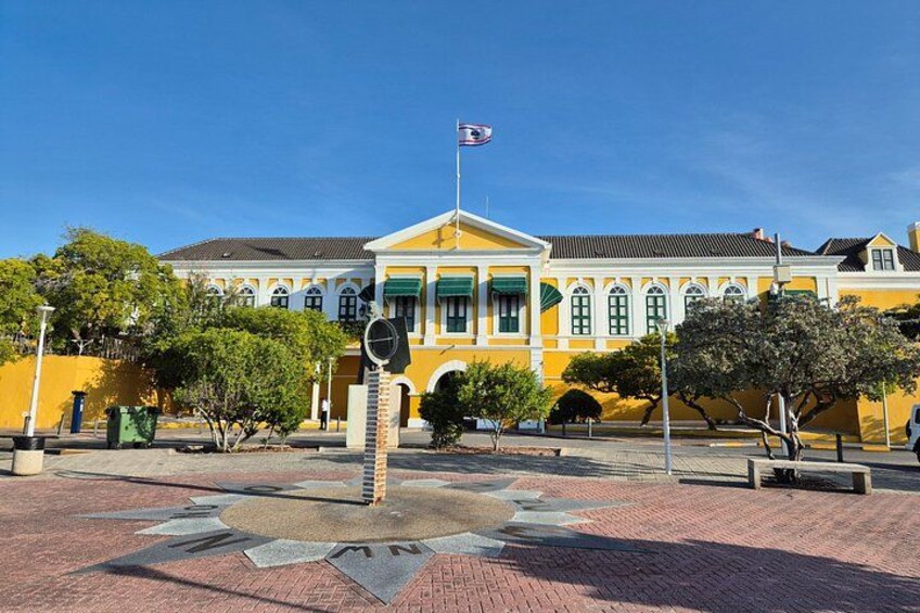 A yellow building with green windows and a flagpole. 1