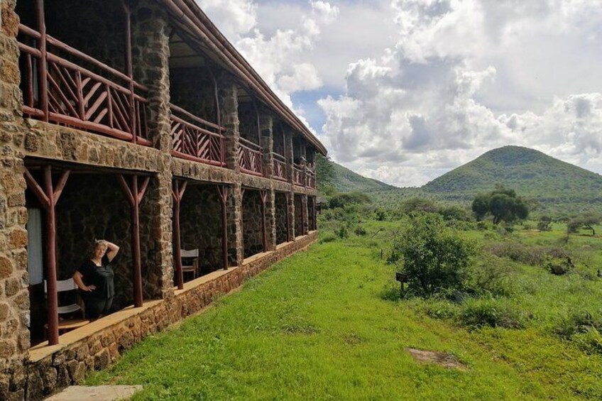 A stone building with a balcony, surrounded by a grassy landscape and hills in the background. 3