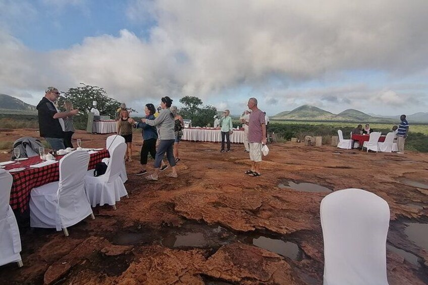 An outdoor event with people dancing, tables set up with white tablecloths, and a mountainous landscape in the background. 5