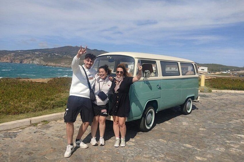 Un groupe de personnes posant devant un vieux camion aménagé, près de la mer. 2