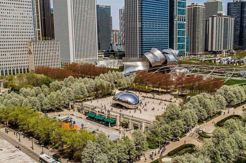 A cityscape with modern architecture, including a distinctive building with a curved roof, surrounded by a park with trees and a plaza. 1