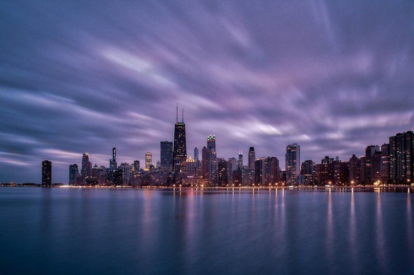 A city skyline at dusk with illuminated buildings reflecting on calm water. 2