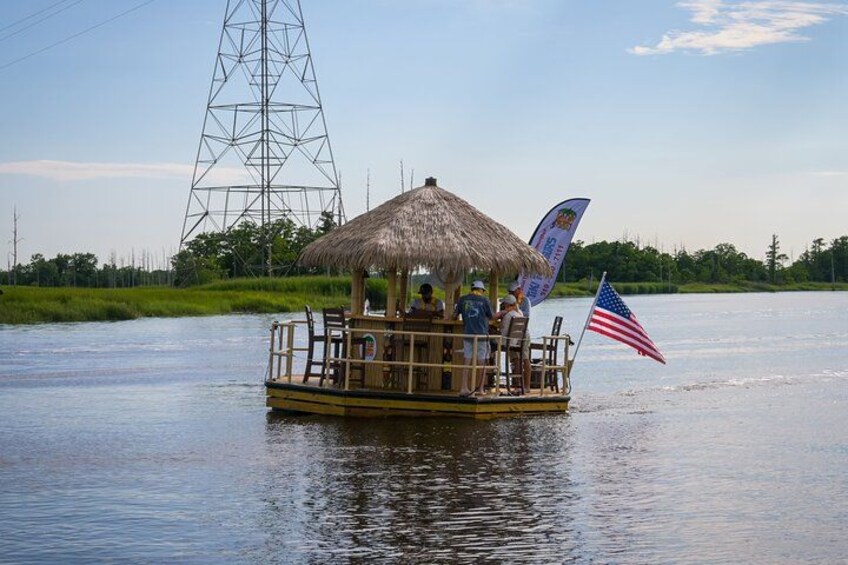Un bateau doté d’un toit de chaume et arborant le drapeau américain, naviguant sur l’eau, avec une tour de ligne à haute tension en arrière-plan. 3