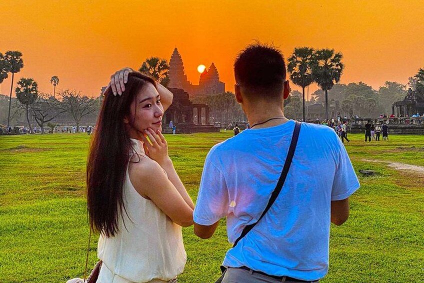Un couple se tient dans un champ d’herbe, avec un temple en arrière-plan, au moment du coucher du soleil. 1