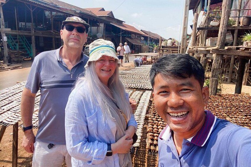 Trois personnes se tiennent dans un marché en plein air, avec des structures en bois et un sol carrelé. 4