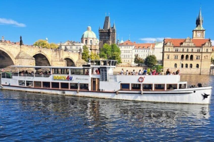 A river cruise boat with passengers, a bridge, and historic buildings in the background. 1