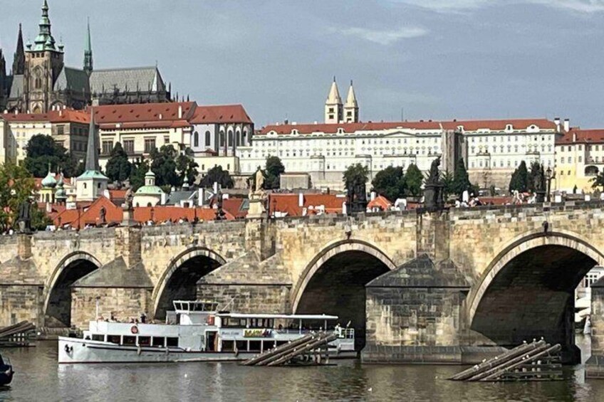 A stone bridge with arches over a river, a boat on the water, and historic buildings in the background. 1